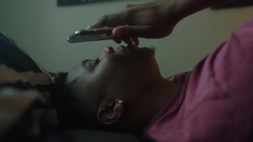 A man lies in bed and holds his phone to his mouth during a call