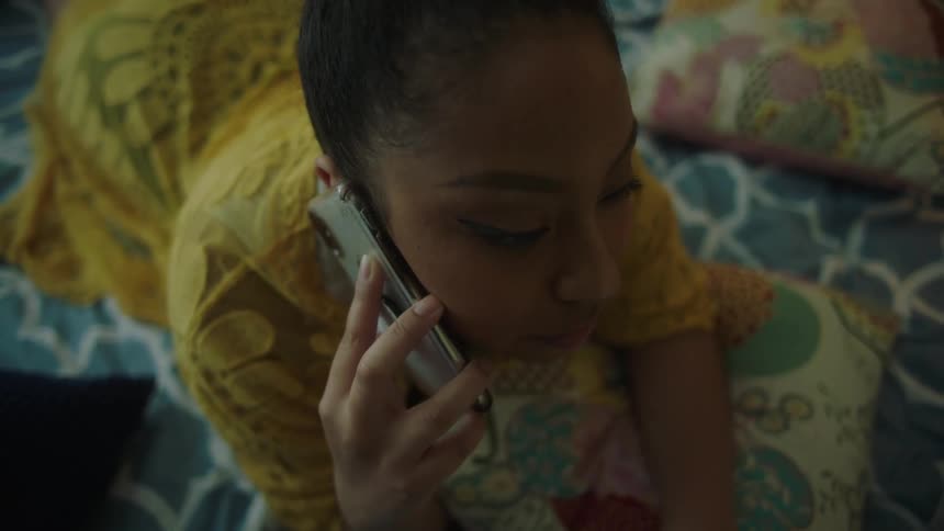 A woman talks on the phone while lying in bed