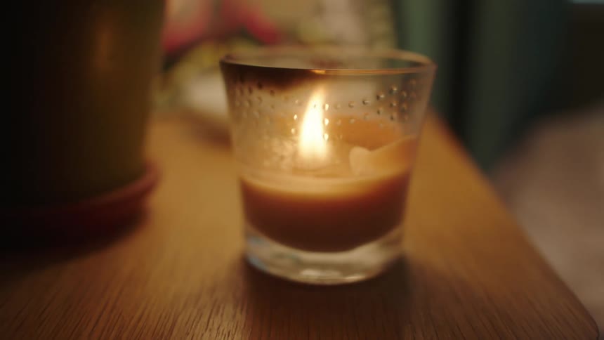 A small candle burns on a wooden tabletop