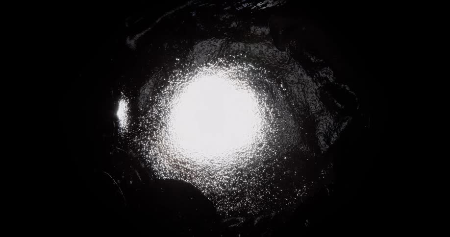 Bright white light shines on the shimmering reflecting surface of a liquid