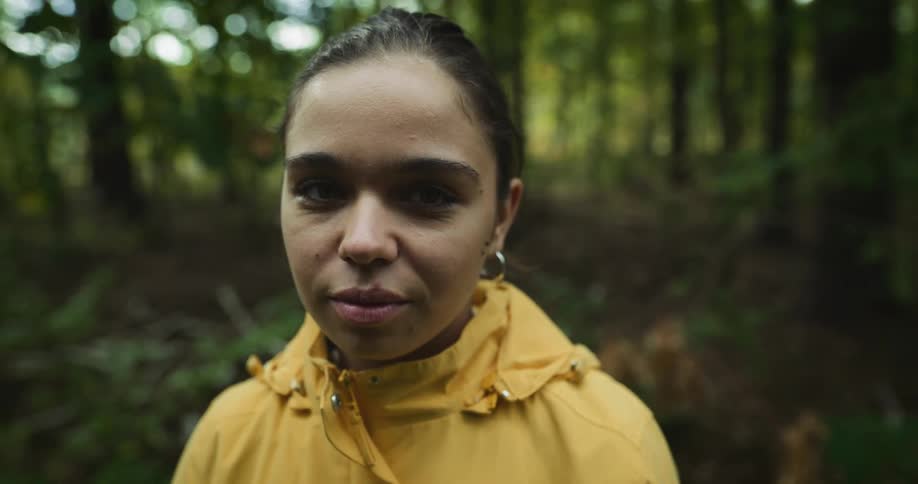 Woman smiles while posing in yellow raincoat in woods