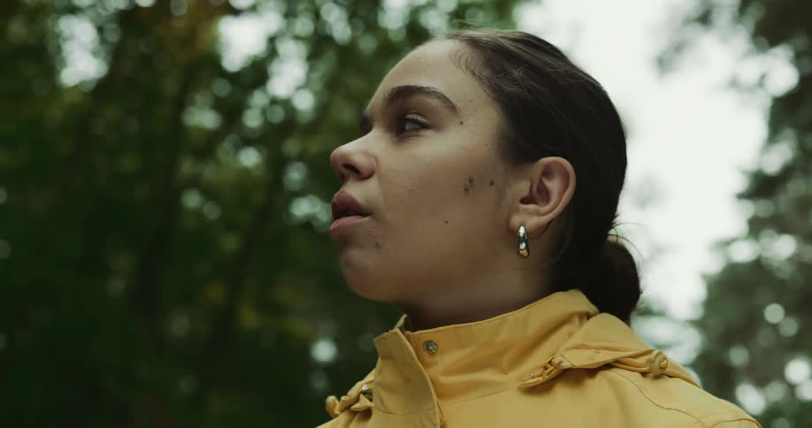 Woman wearing yellow raincoat stands among trees and looks around