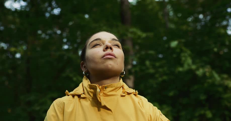 A woman closes her eyes while looking up in the woods