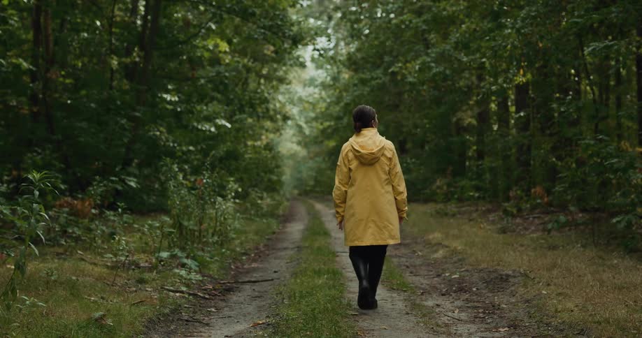 Woman wearing long hooded coat walks along dirt road through woods