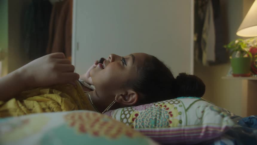 A black female laying on the bed talking on the phone