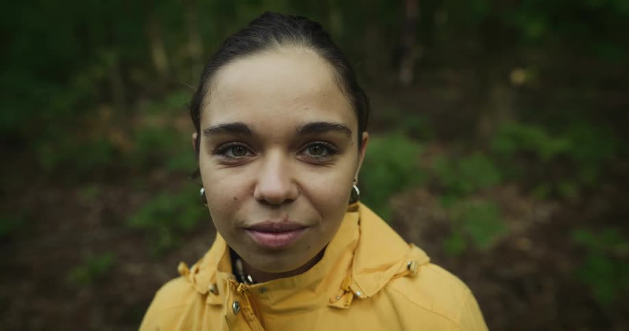 A woman is smiling outdoors in a forest area