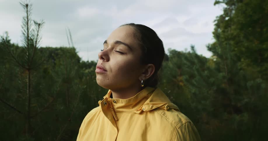 A woman standing in the forest looks up and closes her eyes