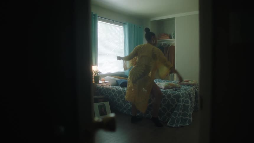 A black female in a yellow outfit dancing in her bedroom