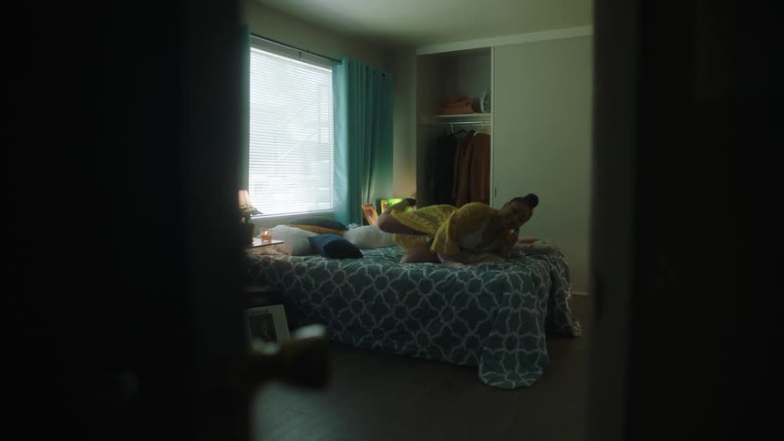 Young woman talking on the phone lays down on the bed in her bedroom at home