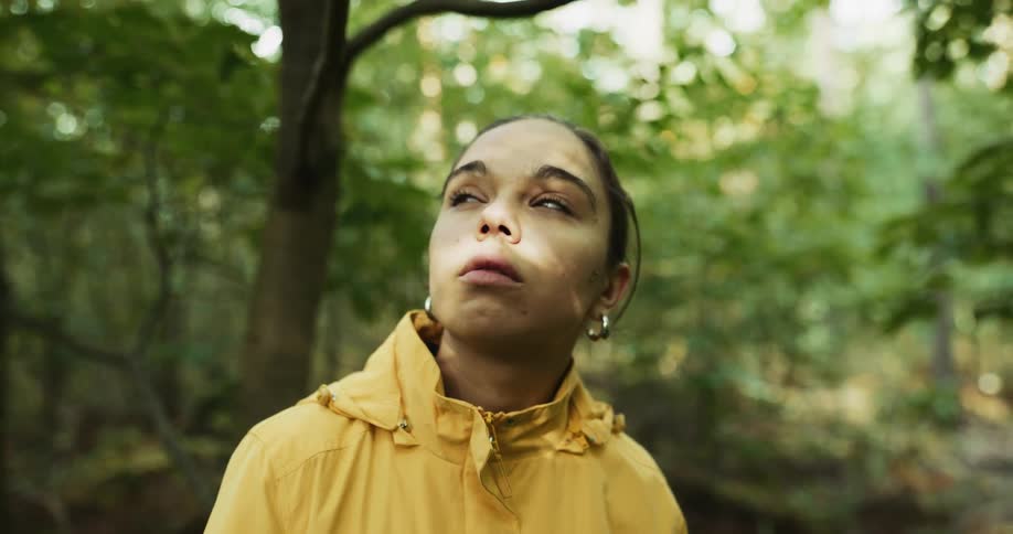 There is a young woman that is staring outdoors in the forest area