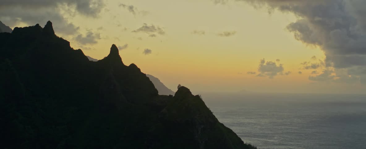 Jagged mountains slope downward toward the tranquil ocean below