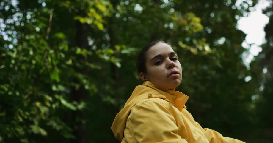 A young female wearing a yellow jacket sitting outside near trees