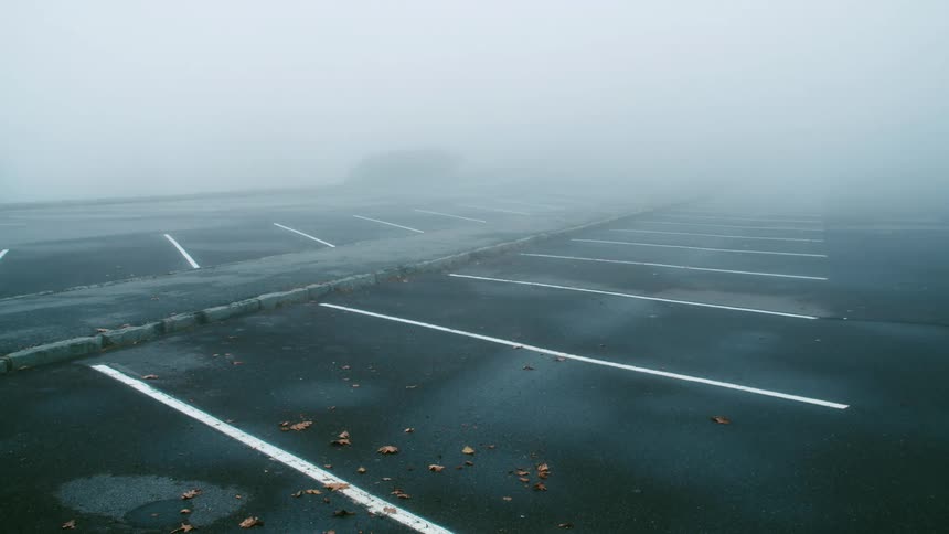 An empty parking lot is located under a dense layer of fog