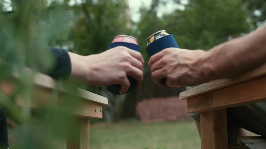 Two people sitting in lawn chairs and drinking cans of beer on a summer day