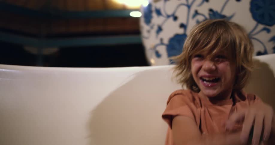 A boy is sitting in a carnival ride bouncing his arms and laughing as he spins in his seat