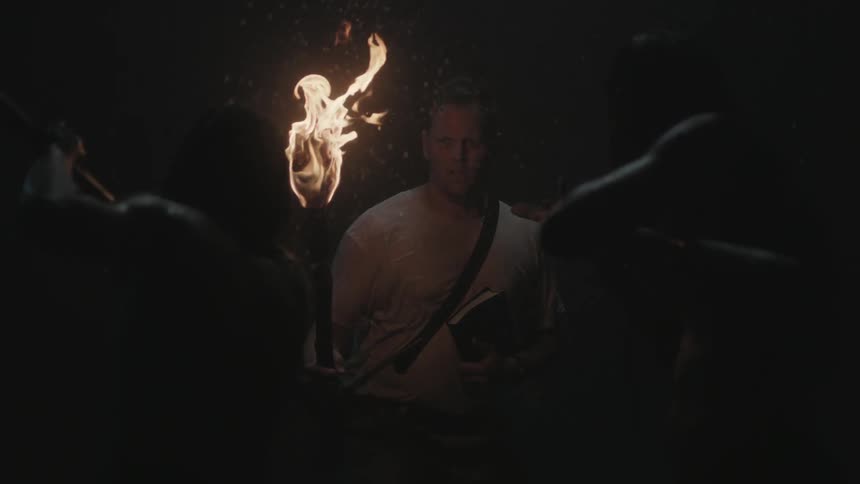 A man carrying a book and a torch is threatened by natives with spears