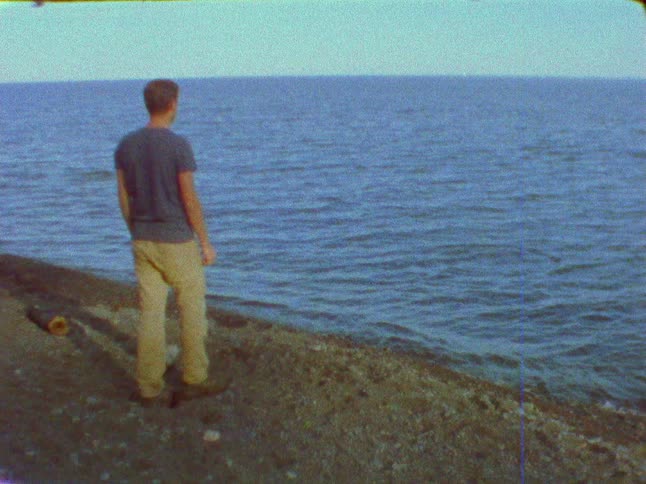 Man standing on shore on a clear day skips rocks