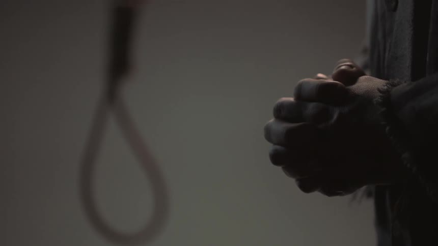A person clasps their hands in front of a noose
