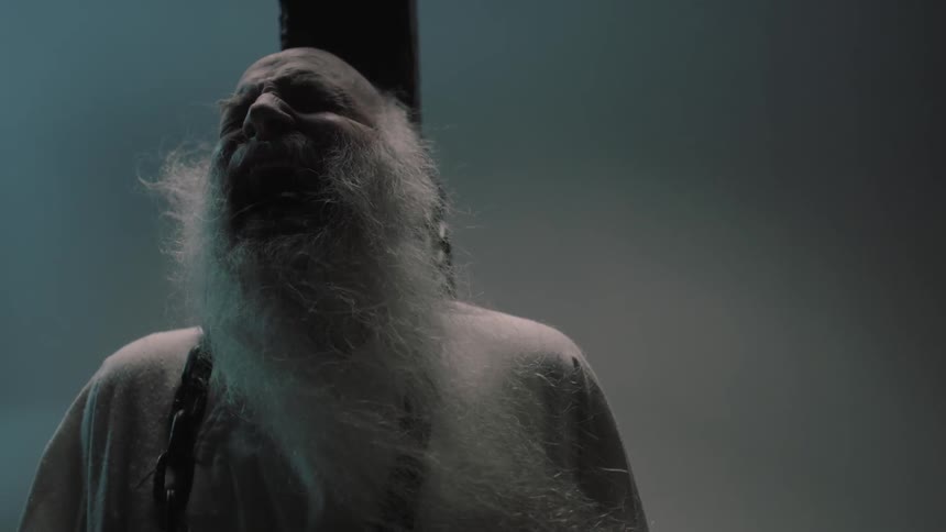 A bearded man screams while being chained to a post