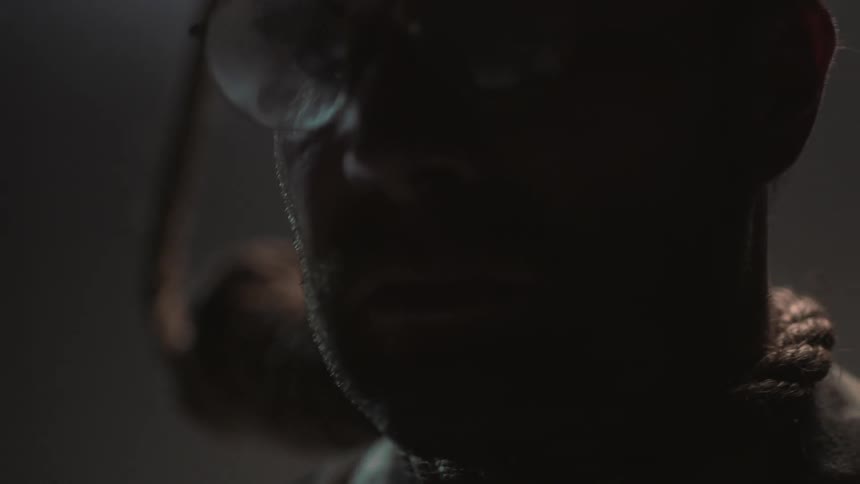 A man in glasses wears a noose in a dark room