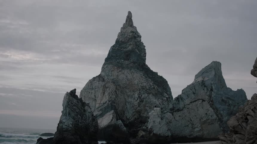A rock outcropping on a beach juts toward the sky