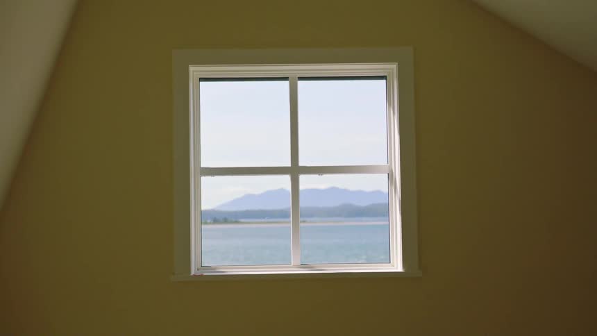 A wall with a window and outside the window is a lake and a mountain in the distance