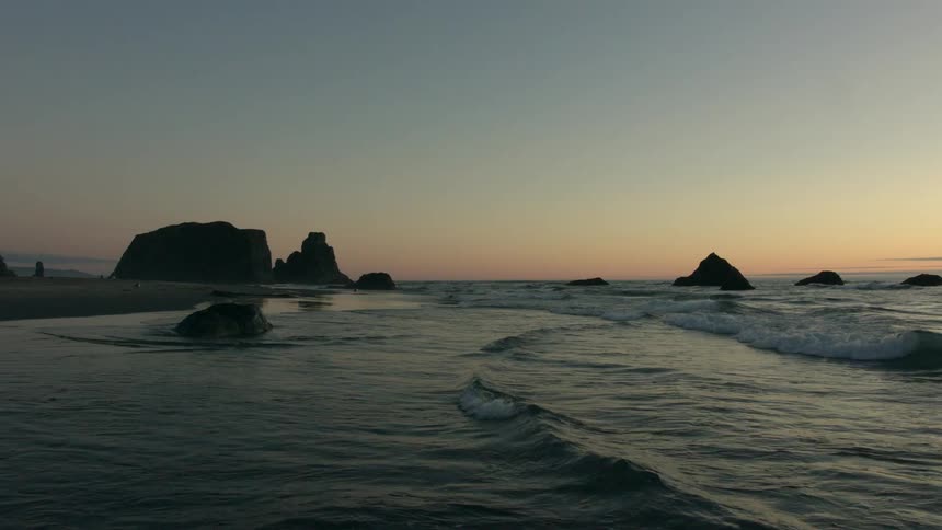 Waves roll into shore splashing on rocks as they move over the sand on the beach under a clear sky