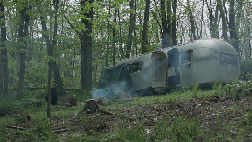 A grey camper in the woods near a campfire