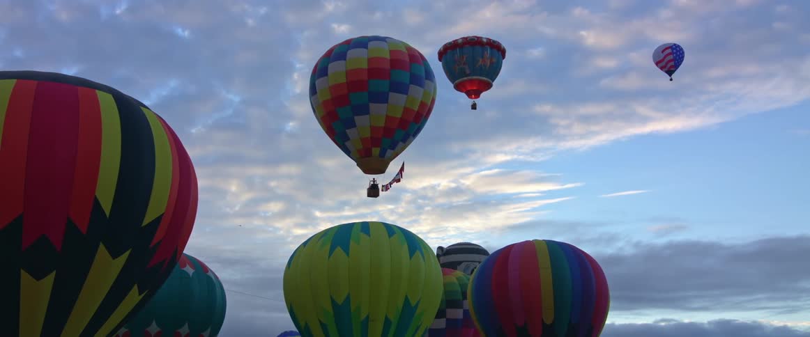 Hot air balloons rise into the cloudy sky