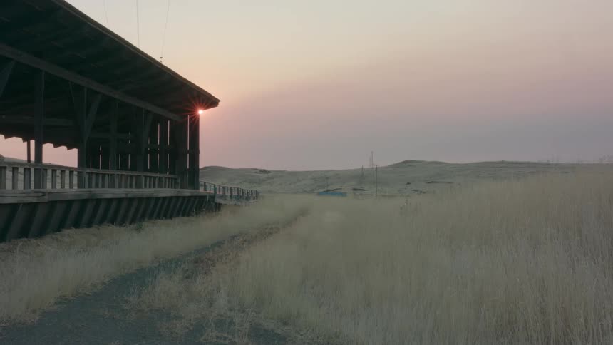Sun setting behind a wooden building in the serene countryside at evening