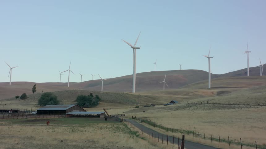 Wind turbines spinning on the hills near a ranch in the countryside at morning