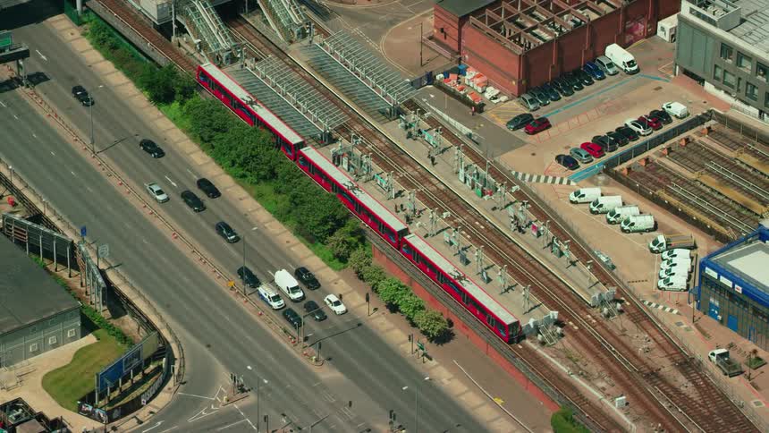 Traffic moves past traffic signals on highway paralleling train tracks near warehouses