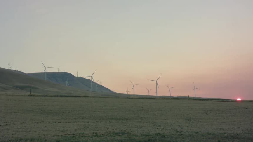 Turbines spinning on a grassy wind farm at sunrise