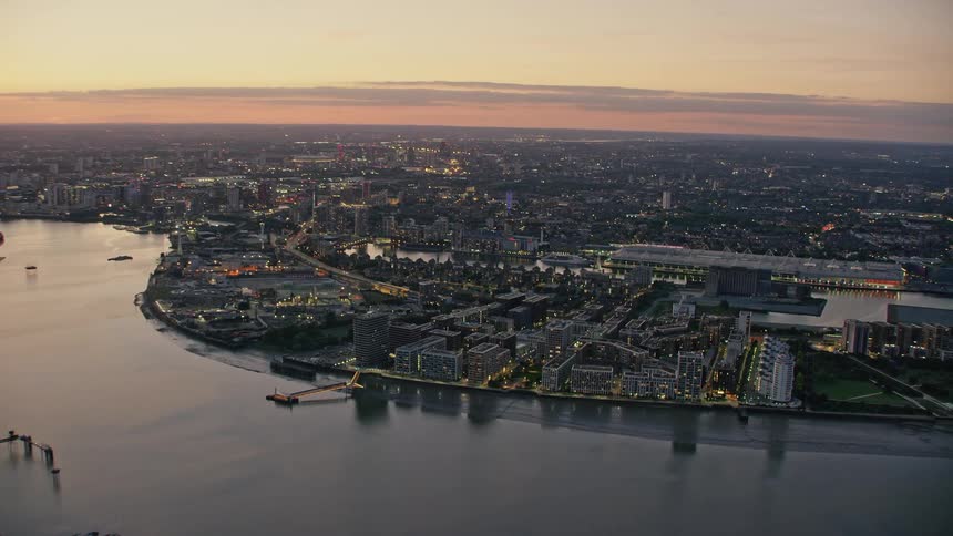 Aerial view of illuminated city skyline next to river at dusk