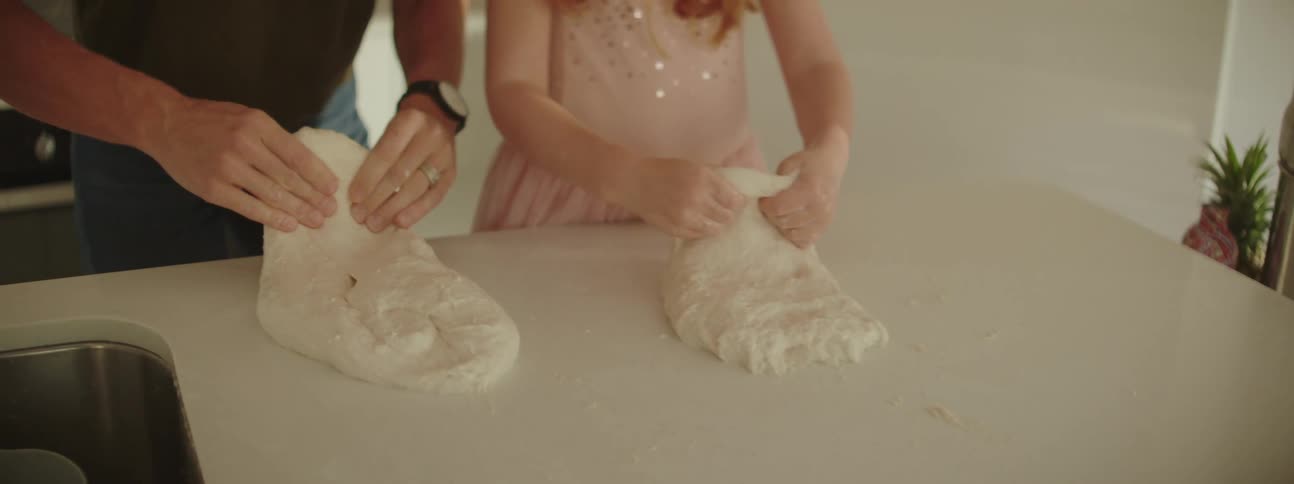 A man and his daughter knead dough on their kitchen counter