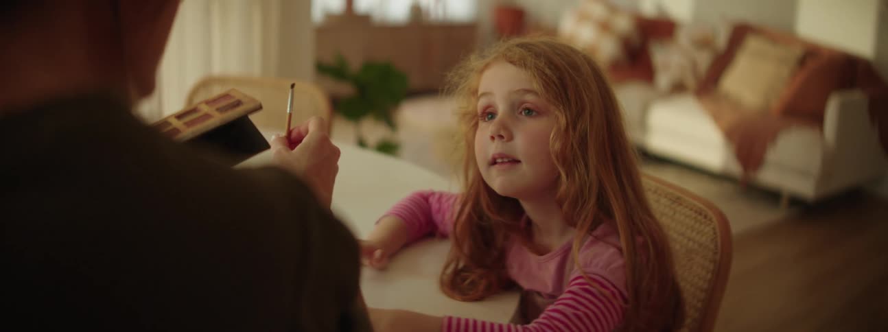 Young daughter smiles as her mother applies makeup to her eyelids