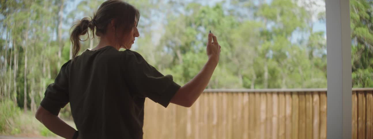 A woman holds her phone out during a video call out her back porch