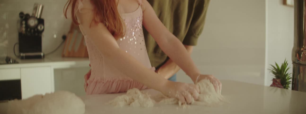 Mother wearing green blouse and jeans and daughter with red hairand pink dress make dough on kitchen island in the kitchen