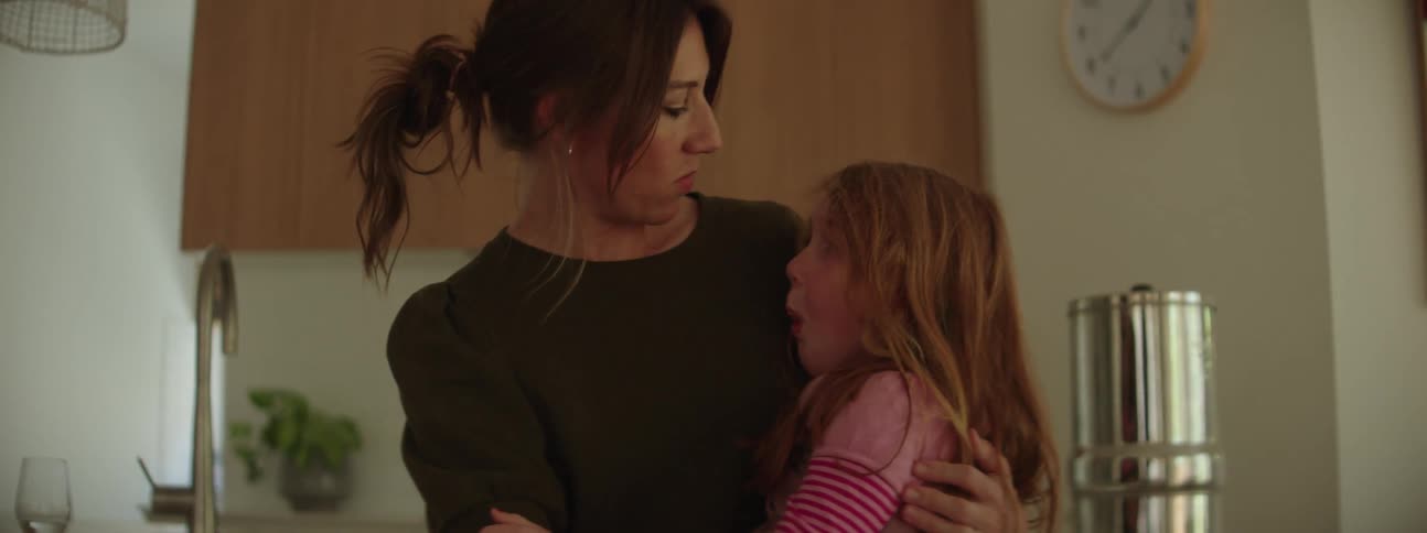 A woman is standing in the kitchen hugging her little girl and comforting her