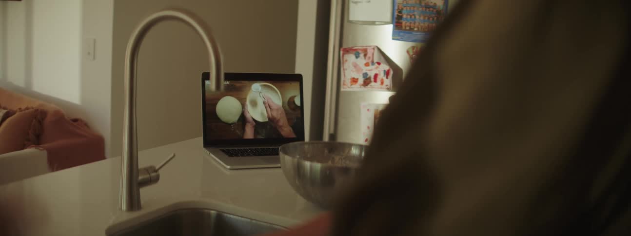 Mother with ponytail gray t shirt and daughter with red hair watches laptop in the kitchen