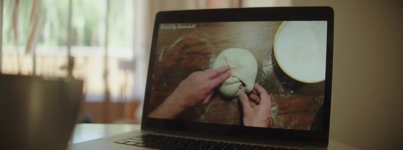 Laptop on kitchen counter playing a video of man kneading dough