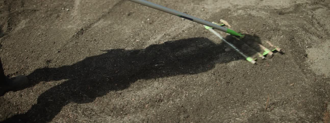 Shadow of a woman using a rake to spread gravel on the ground