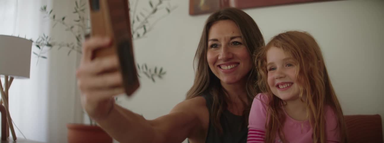 Happy mother and daughter share kisses while taking a selfie at home
