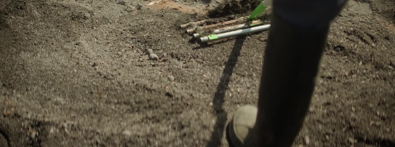 A woman is outside spreading soil in her yard as her young daughter plays and tries to help