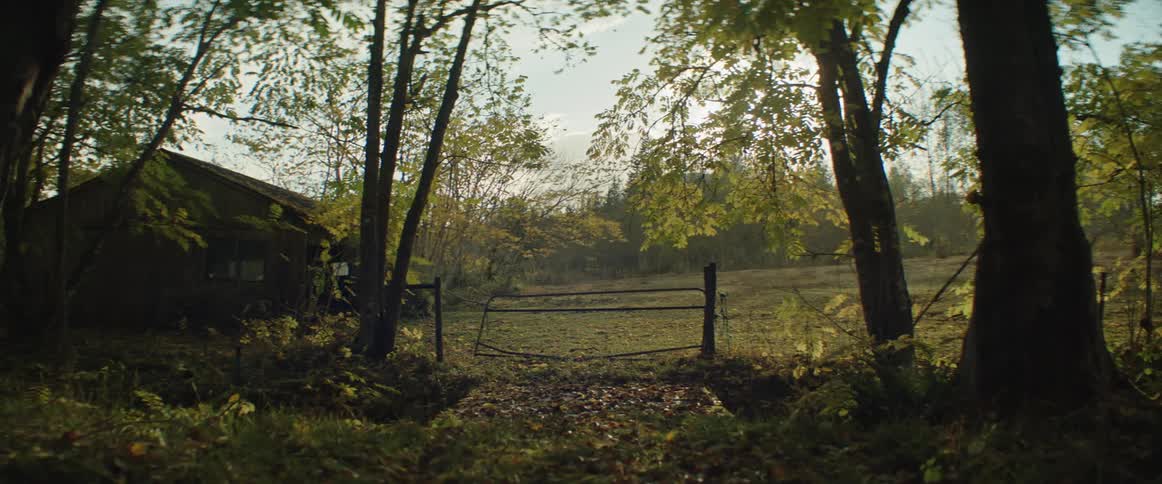 An old rural fence leads into a field with a nearby stable with fall colors present