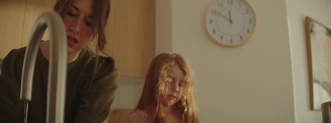 A woman is standing at the kitchen counter with her young daughter laughing as she works with dough