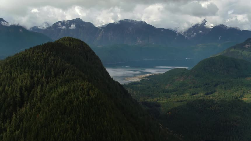 Aerial view of a forested mountain with a distant lake being revealed