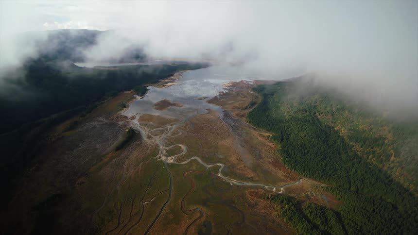 Clouds part to reveal river estuaries flowing from a lake in the mountainous wilderness