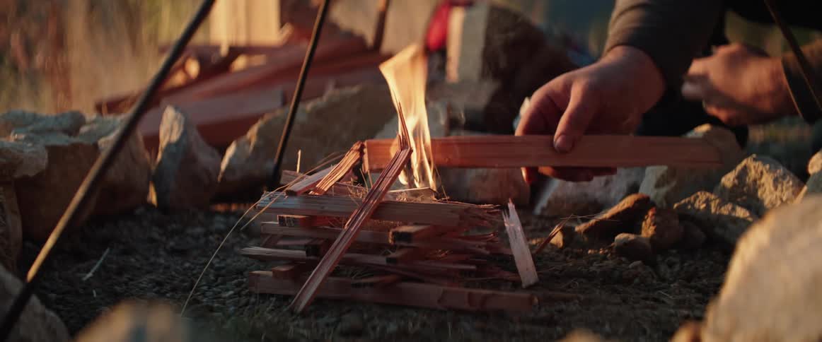 Close up of a man using a piece of wood as kindling to start a campfire