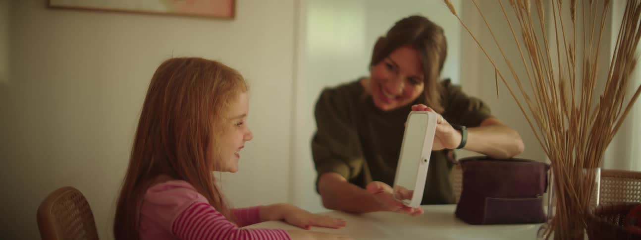 A mother and daughter sitting at a table looking at a tablet